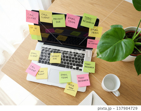 付箋でタスクが溢れたノートパソコンとデスクワークの忙しさを表すイメージ 137984729