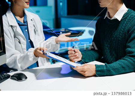 Doctor explains medical form as patient signs consent in modern clinic. Healthcare, insurance, medical consultation, diagnosis, treatment, documentation concept. 137986013