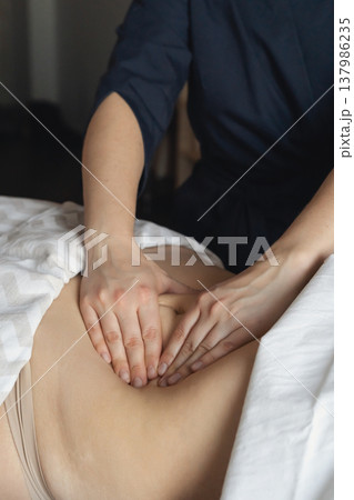 Woman receiving relaxing stomach massage from a therapist in a tranquil spa room with warm candlelight. Promoting wellness and health Woman receiving relaxing stomach massage from a therapist in a tranquil spa room with warm candlelight. Promoting wellness and health 137986235
