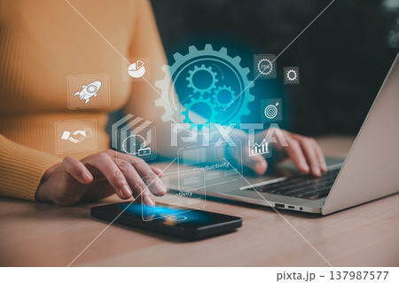 Worker using smartphone and laptop with holographic gears and productivity icons, illustrating workflow automation, business growth, digital efficiency, performance tracking and smart management. Worker using smartphone and laptop with holographic gears and productivity icons, illustrating workflow automation, business growth, digital efficiency, performance tracking and smart management. 137987577