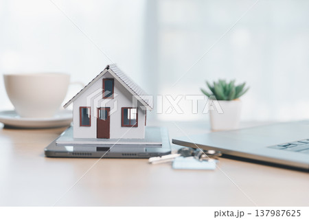 Home buying and mortgage planning concept for real estate investment and insurance, featuring a miniature house, keys, calculator, pen and contract on a bright desk in a modern office. real estate 137987625