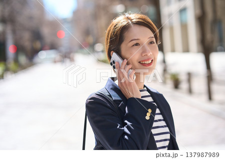 街を歩きながらスマートフォンで通話する30代日本人ビジネスウーマン 137987989