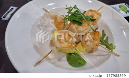 Delicious Shrimp Skewers Served on a Gourmet Plate with Fresh Greens and Flavorful Sauce Delicious Shrimp Skewers Served on a Gourmet Plate with Fresh Greens and Flavorful Sauce 137988869