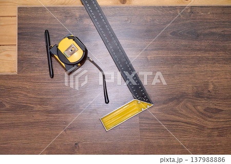 Precision Tools for Floor Measurement: Tape Measure and Square on Wood Flooring Surface 137988886