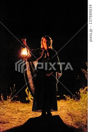 Portrait of a young woman in a medieval cloak holding a lantern against a black background Portrait of a young woman in a medieval cloak holding a lantern against a black background 137989834