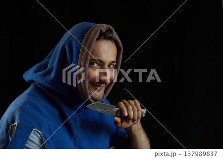 Portrait of a smiling man in a medieval hood holding a knife Portrait of a smiling man in a medieval hood holding a knife 137989837