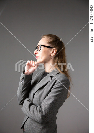 A profile portrait of a woman with glasses and long hair in a business suit, lost in thought and touching her chin A profile portrait of a woman with glasses and long hair in a business suit, lost in thought and touching her chin 137989842