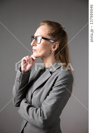 A profile portrait of a woman with glasses and long hair in a business suit, lost in thought and touching her chin. Vertical photo A profile portrait of a woman with glasses and long hair in a business suit, lost in thought and touching her chin. Vertical photo 137989846