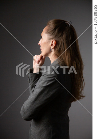 A portrait of a woman in a business suit, deep in thought, holding her chin in her hand A portrait of a woman in a business suit, deep in thought, holding her chin in her hand 137989865