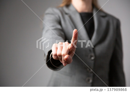 A portrait of a woman with glasses and long hair, wearing a business suit, extending her hand forward with her index finger raised. A prohibiting gesture. 137989868
