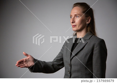A portrait of a woman in a business suit, extending her hand forward with her palm turned sideways. A welcoming gesture inviting a handshake A portrait of a woman in a business suit, extending her hand forward with her palm turned sideways. A welcoming gesture inviting a handshake 137989879