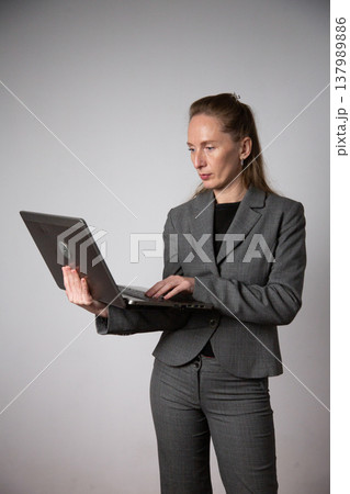 Vertical photo. A woman in a business suit holding a laptop 137989886