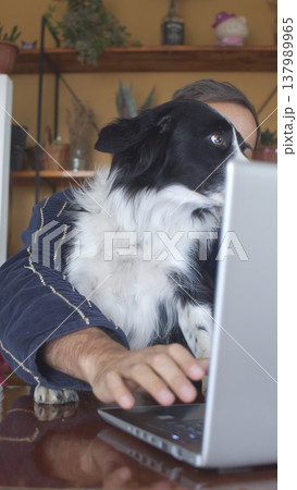 A portrait of a man in a dressing gown with a dog in front of a laptop. Vertical photo 137989965