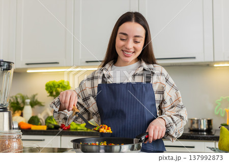 Young woman tasting vegetarian stir fry in kitchen while cooking healthy homemade dinner at home hot Young woman tasting vegetarian stir fry in kitchen while cooking healthy homemade dinner at home hot 137992873
