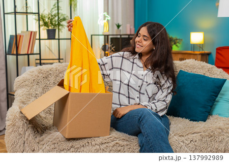 Indian woman unboxes delivery box finds new scarf smiles joy celebrating successful online shopping Indian woman unboxes delivery box finds new scarf smiles joy celebrating successful online shopping 137992989