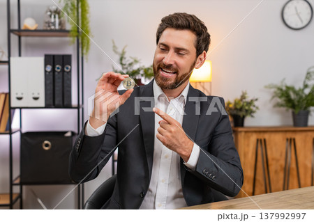 Middle-aged businessman shows Bitcoin golden coin spins it recommending crypto investment to viewers Middle-aged businessman shows Bitcoin golden coin spins it recommending crypto investment to viewers 137992997