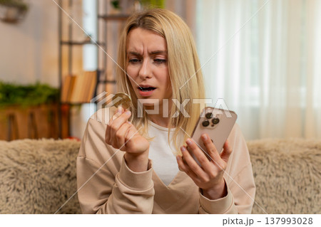 Adult woman checking bitcoin drop on smartphone at home, shaking head in disappointment frustration Adult woman checking bitcoin drop on smartphone at home, shaking head in disappointment frustration 137993028