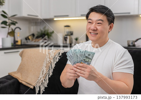 Asian man counts cash dollars smiles makes money sign and plans invest purchase bonus salary savings 137993173