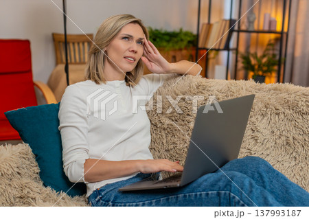 Woman massaging temples on sofa at home, feeling tired from long work on laptop headache discomfort Woman massaging temples on sofa at home, feeling tired from long work on laptop headache discomfort 137993187