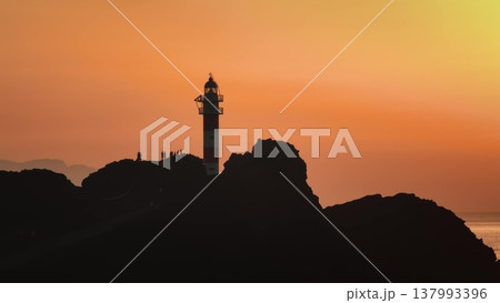 Tourists silhouette against vibrant sunset at Punta de Teno lighthouse, showcasing a stunning coastal view under bright orange sky. Tenerife, Canary Islands. Drone flight panorama Tourists silhouette against vibrant sunset at Punta de Teno lighthouse, showcasing a stunning coastal view under bright orange sky. Tenerife, Canary Islands. Drone flight panorama 137993396
