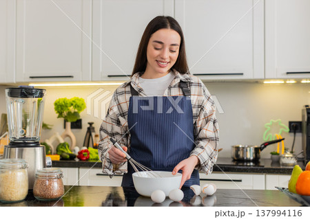 Young woman cracking eggs in kitchen bowl preparing simple breakfast omelet or baking dough at home 137994116