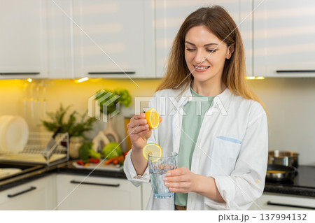 Middle-aged woman adding lemon to water in kitchen for detox hydration and healthy diet routine plan Middle-aged woman adding lemon to water in kitchen for detox hydration and healthy diet routine plan 137994132