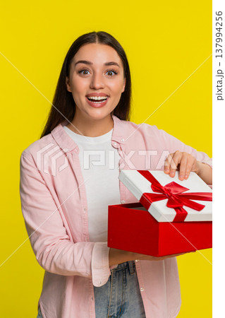 Woman opening birthday gift box with surprised happy expression joyful emotional reaction to present Woman opening birthday gift box with surprised happy expression joyful emotional reaction to present 137994256