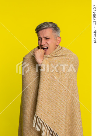 Adult man wrapped in blanket coughing with tired sick face showing flu symptoms cold virus illness Adult man wrapped in blanket coughing with tired sick face showing flu symptoms cold virus illness 137994257