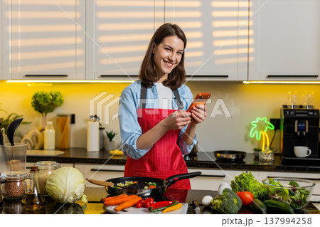 Young woman smiling at smartphone in kitchen planning healthy diet meal prep for weight loss at home Young woman smiling at smartphone in kitchen planning healthy diet meal prep for weight loss at home 137994258