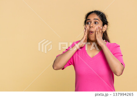Indian woman with shocked expression, eyes wide open and hands on face isolated on beige background Indian woman with shocked expression, eyes wide open and hands on face isolated on beige background 137994265