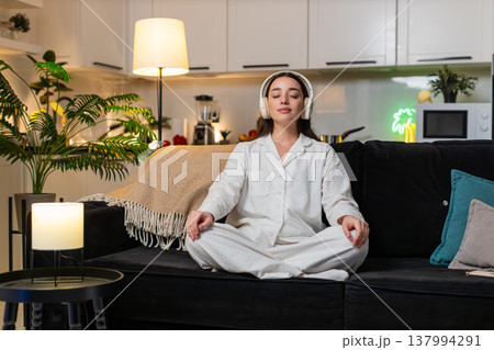 Young woman in headphones meditates to rain sounds deep breathing calm mind quiet mood evening sleep Young woman in headphones meditates to rain sounds deep breathing calm mind quiet mood evening sleep 137994291