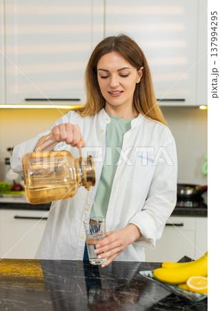 Middle-aged woman drinking water in home kitchen feeling satisfied for daily diet hydration wellness Middle-aged woman drinking water in home kitchen feeling satisfied for daily diet hydration wellness 137994295