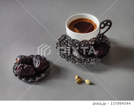 A cup of coffee sits next to dried dates and cardamom seeds. A cup of coffee sits next to dried dates and cardamom seeds. 137994544