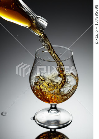 The amber-gold strong alcoholic beverage is poured into a glass. The amber-gold strong alcoholic beverage is poured into a glass. 137995698