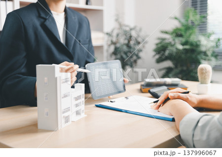 Real estate agent presenting property data on digital tablet to client beside house model in office, concept of home buying, mortgage planning, investment analysis and residential consultation. Real estate agent presenting property data on digital tablet to client beside house model in office, concept of home buying, mortgage planning, investment analysis and residential consultation. 137996067