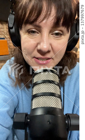 woman with headphones sits in front of a microphone and speaks  137997679