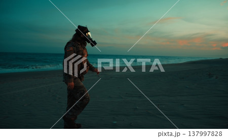 Soldier walks on beach contaminated by radiation from nuclear attack at sunset 137997828