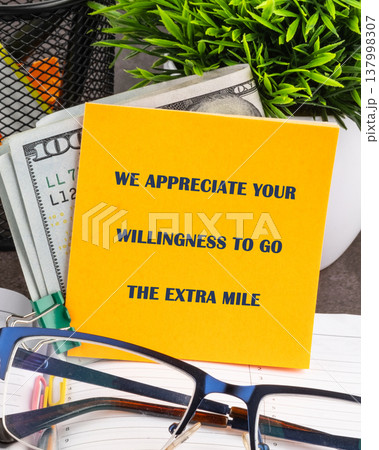 A vibrant yellow note expressing gratitude for exceptional effort rests amidst crisp 100 dollar bills, green plant, and eyeglasses on a clean office desk A vibrant yellow note expressing gratitude for exceptional effort rests amidst crisp 100 dollar bills, green plant, and eyeglasses on a clean office desk 137998307