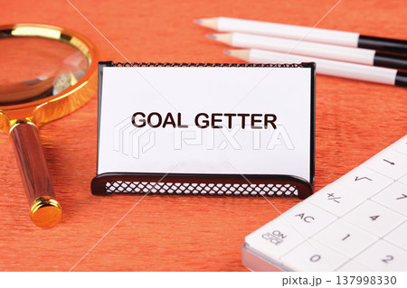 Goal Getter card on bright orange desk with magnifying glass, pencils, calculator. Tools for dedication strategic planning for success Goal Getter card on bright orange desk with magnifying glass, pencils, calculator. Tools for dedication strategic planning for success 137998330