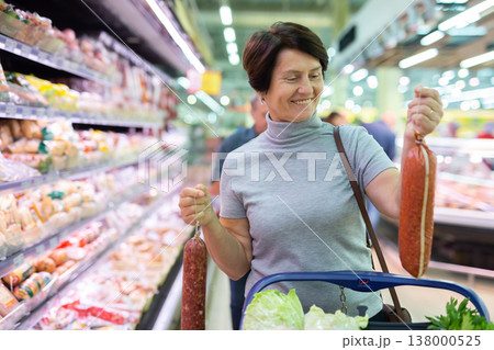 Elderly woman chooses sausage in supermarket Elderly woman chooses sausage in supermarket 138000525