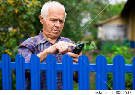 Elderly man writes message on smartphone. Concept of using digital gadgets by elderly Elderly man writes message on smartphone. Concept of using digital gadgets by elderly 138000532
