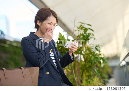 スマートフォンを見て喜ぶ30代日本人ビジネスウーマン スマートフォンを見て喜ぶ30代日本人ビジネスウーマン 138001305