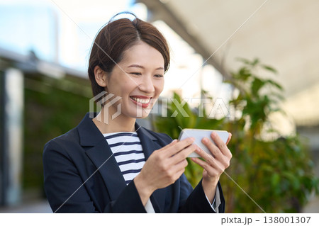 スマートフォンを見て喜ぶ30代日本人ビジネスウーマン スマートフォンを見て喜ぶ30代日本人ビジネスウーマン 138001307
