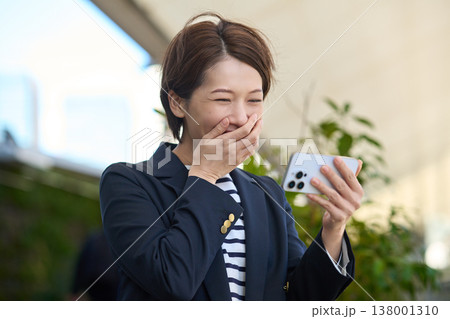 スマートフォンを見て喜ぶ30代日本人ビジネスウーマン スマートフォンを見て喜ぶ30代日本人ビジネスウーマン 138001310