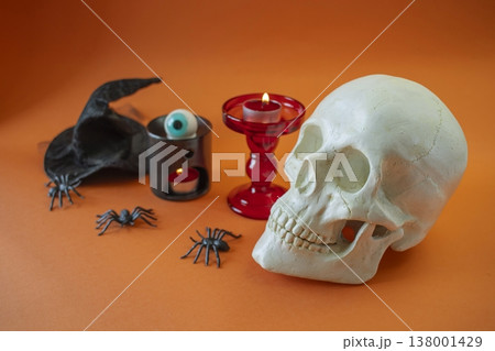 Halloween decorations with skull, candles, witch hat and spiders on orange background. Interior decoration for Halloween. Halloween decorations with skull, candles, witch hat and spiders on orange background. Interior decoration for Halloween. 138001429