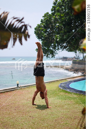 Man holding handstand on grass near ocean in tropical setting Man holding handstand on grass near ocean in tropical setting 138001536