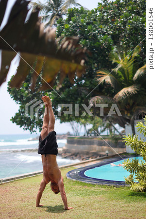 Man holding handstand on grass near ocean in tropical setting Man holding handstand on grass near ocean in tropical setting 138001546