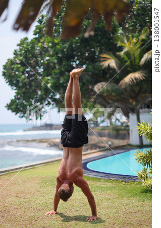 Man holding handstand on grass near ocean in tropical setting Man holding handstand on grass near ocean in tropical setting 138001547