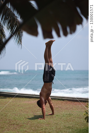 Man holding handstand on grass near ocean in tropical setting 138001571