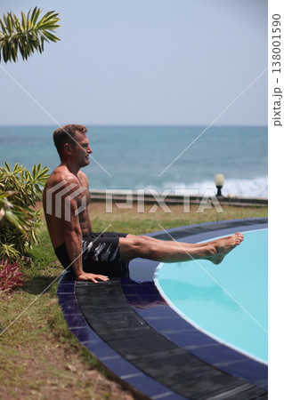 Athletic man performing L-sit exercise near pool with ocean view Athletic man performing L-sit exercise near pool with ocean view 138001590